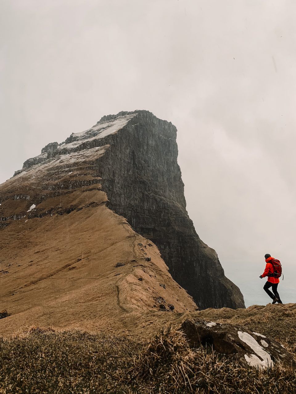 Polle in a red jacket walking along a ridge below a steep cliff